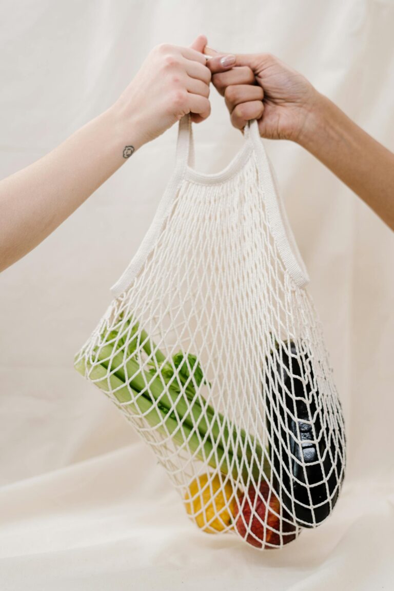Hands holding a mesh bag filled with fresh vegetables, promoting sustainable shopping practices.